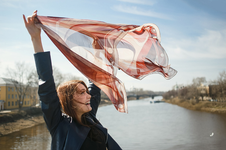 Cheerful girl holding a scarf, waving in the wind. Concept of spring, freedom, travel and windy weatherの写真素材