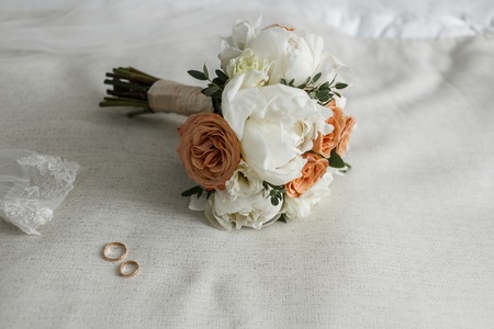Bridal Bouquet With Beige and Creamy roses and Bridal rings on White Bedの写真素材