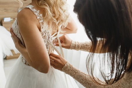 Bridesmaid ties a wedding lace dress to the brideの写真素材