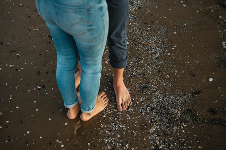 A young couple is having fun and walking on the sea coastline. Legs close up. Romantic date on the beachの写真素材