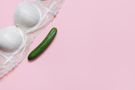 Erotic chat, dating, virtual sex concept. White bra and big cucumber on a pink background. Minimalistic Flat lay, top viewの写真素材