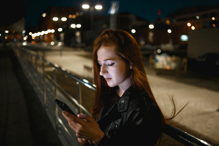 Young redhead woman using mobile phone on night streetの写真素材