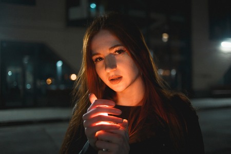 Young redhead woman with a burning lighter in the night cityの写真素材