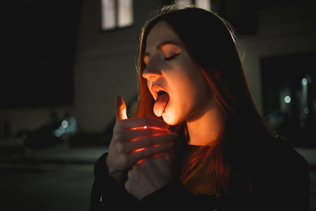 Young redhead woman lighting a lighter and showing tongue, eating fire. Nightの写真素材
