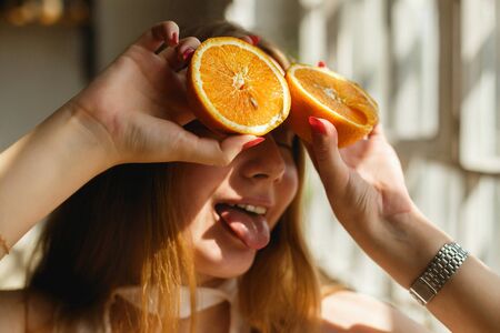 Beauty Ginger Girl takes Juicy Oranges. Beautiful Joyful teen girl Holding Orange Slices and showing tongue, laughing emotionsの写真素材