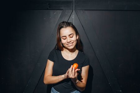 Happy young woman with mandarin friendly looking to camera at beige background. She clothed in black t-shirtの写真素材