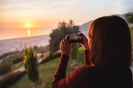 Traveler woman use mobile phone take a photo of beautiful of sunset nature at top of mountain sea view.の写真素材