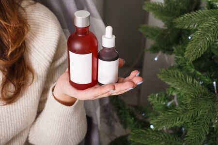 Female hand with a two jar of tonic on fir tree backgroundの写真素材