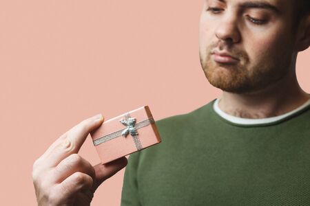 A young stylish man holds a beautiful pink box with a gift for Valentines Day against the backdrop of a pink wallの写真素材