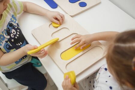 Arkhangelsk, Russia - February, 2, 2019: Children collecting colorful figurine from a colored wooden puzzles on white board. Preschool development and education of childrenのeditorial素材