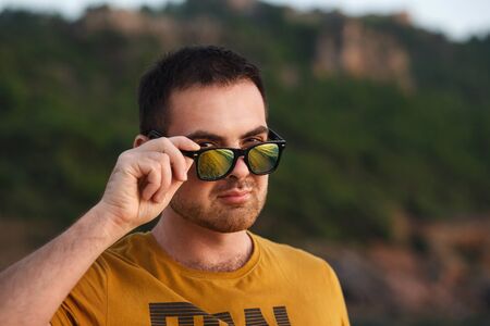 Attractive man in yellow glasses relaxes on the beach at sunset