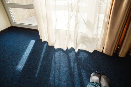 Close up carpet with daylight shining through the white transparent curtain. Feet in socks on foreground.の写真素材