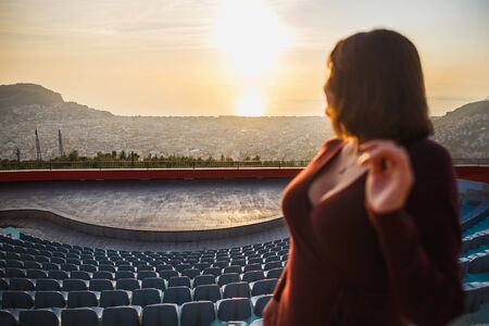 Mountain amphitheatre in Alanya, Turkey. A stunning view of the sunset cityscape and the sea. Busty girl in a dress in the foreground. Focus on the landscape.の写真素材