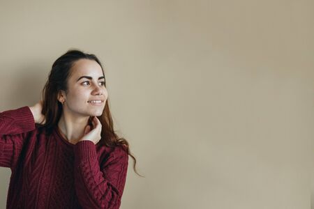 Happy young latin woman in claret sweater posing at beige background. Friendly looking. Copy space.の写真素材