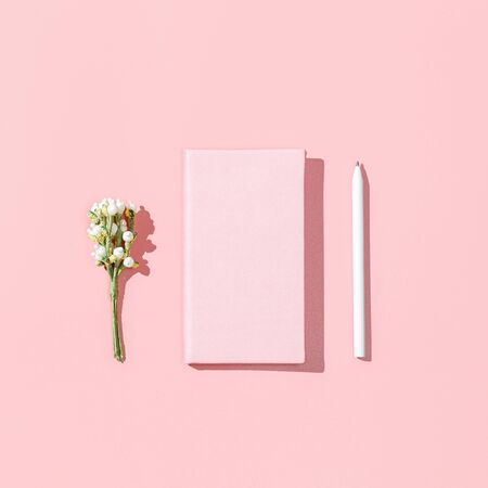 Minimalistic card mockup with empty pink notebook, white pen, blossom flower branch on pink background. Spring feminine blogger concept. Flat lay, square image, top view, copy spaceの写真素材