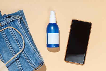 Delivery package, phone, jeans and blue sanitizer on yellow background. Concept online store,...