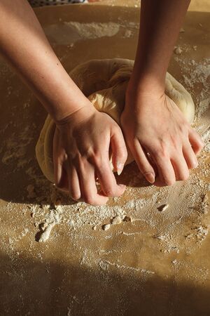 Womans hands knead dough on a table in warm sunlight