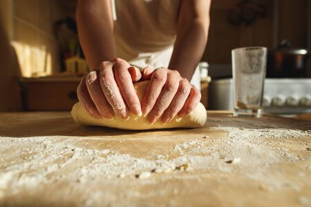 Womans hands knead dough on a table in warm sunlight