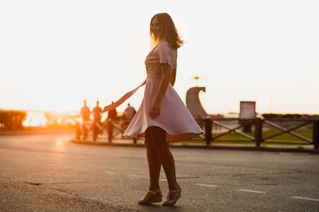 Beautiful joyful girl in the dance on road the sunset . A delicate pink dress flutters beautifully. Dynamic silhouetteの写真素材