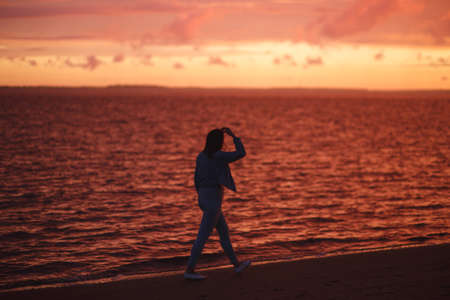 Woman walks alone on the beach and looks at the colorful sunset after the rainの写真素材