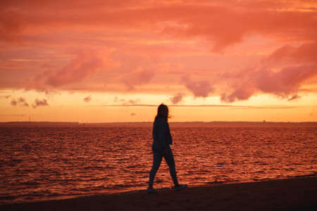 Woman walks alone on the beach and looks at the colorful sunset after the rain. Beautiful scenery,...