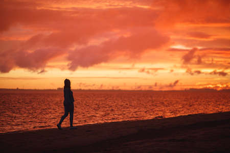 Woman walks alone on the beach and looks at the colorful sunset after the rainの写真素材