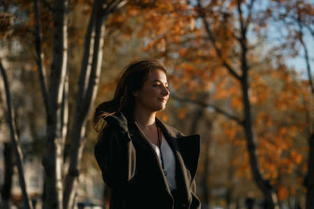 Outdoor fashion photo of young beautiful lady in red scarf and dark grey coat surrounded autumn...