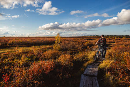 Young man on a bicycle in red colors of autumn tundra