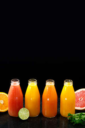 Mix of orange and yellow colored fruits and juices on black background. Composition of tropical and mediterranean fruits. Oranges, grapefruits, limes. Vertical imageの写真素材