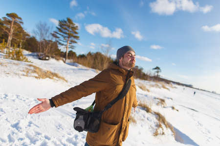 Portrait, of young carefree stylish man with a beard dressed in beige winter jacket with a hood. Winter and frost themeの写真素材