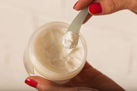 Womens hands put the cream from a large jar into a small one with a spatula. Closeup texture of creamの写真素材