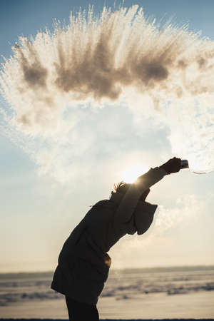 The girl has fun in the winter splashes boiling water from the thermos on the strong frost. The concept of winter fun, severe frostsの写真素材