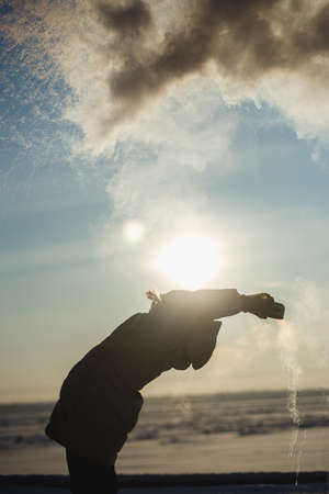 The girl has fun in the winter splashes boiling water from the thermos on the strong frost. The concept of winter fun, severe frostsの写真素材