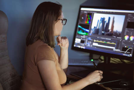 Woman video creator mounts video at desktop. Home workstationの写真素材