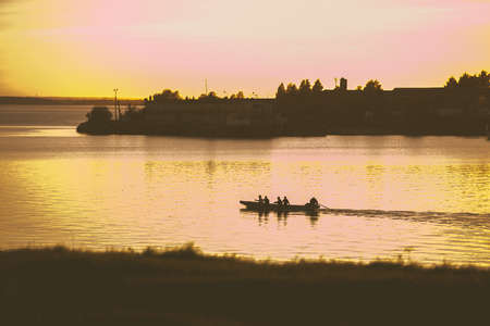 The silhouette of a canoe or a kayak floating on the river at sunset. Warm toning