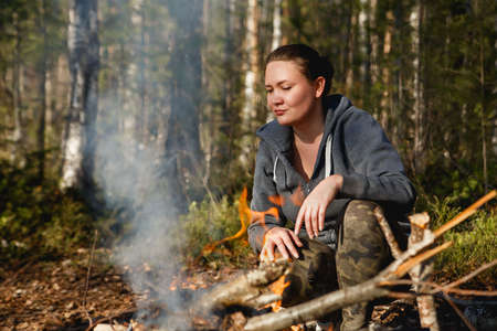 Girl lights a fire for cooking in the spring forestの写真素材