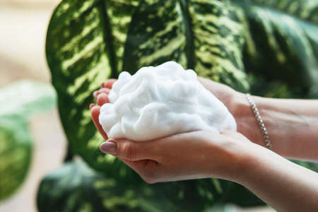 Hands washing gesture with foaming hand soap on green leaves
