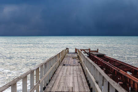 Old pier and atmospheric stormy sea with a rich blue color of water and clouds. Minimalistic storm landscapeの写真素材