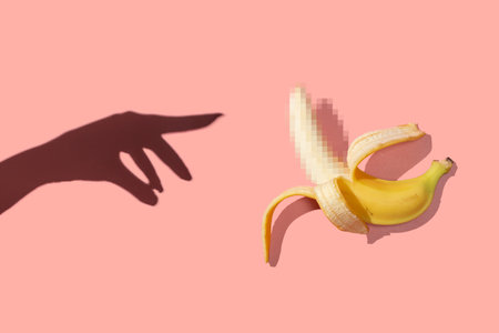 Symbol of the penis in the form of a ripe banana with blurred censored squares and female hand on a pink backgroundの写真素材