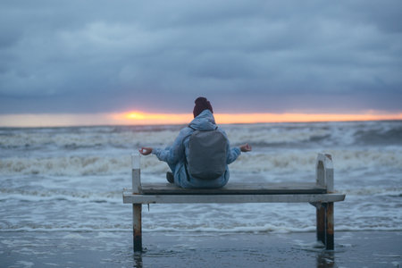 Lonely girl sitting on a bench by the sea in a winter storm. High quality photo.の写真素材