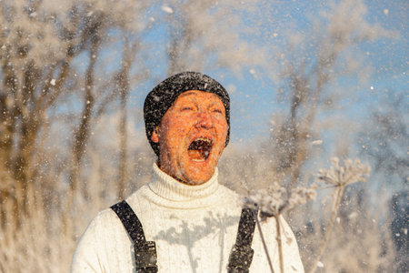A cheerful, brave man in black clothes having fun on the white snow in winter and screams with...