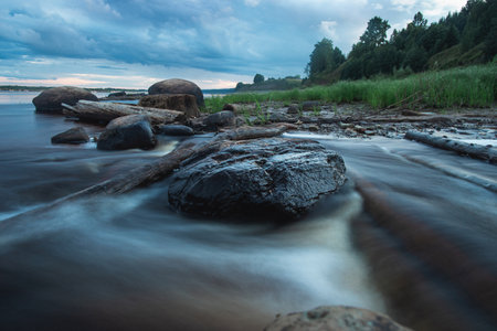 A serene river flowing amidst rocky shores with trees in the background, under a clear sky with...