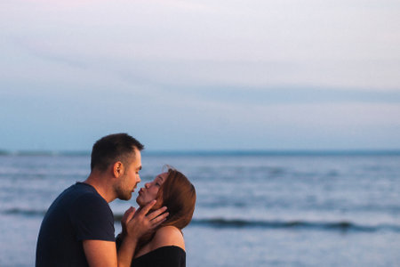 A happy couple shares a kiss on the beach under the blue sky and white clouds. People are watching as the ocean water glistens in the sunの写真素材