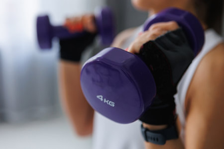 A woman in sports uniform is holding two purple dumbbells in her hands, showcasing her strength and commitment to fitness and exerciseの写真素材