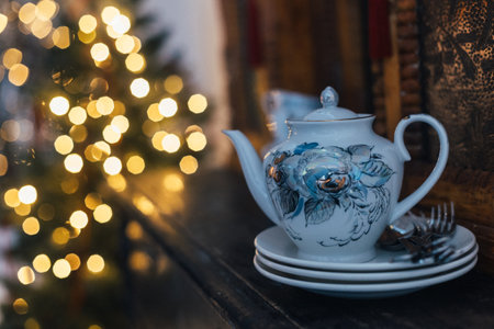 A beautiful teapot and elegant plates are thoughtfully arranged on a table positioned in front of a splendidly decorated Christmas treeの写真素材