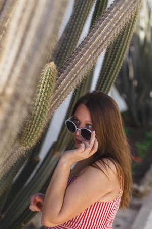 A fashionable woman poses next to a cactus, showcasing vibrant summer vibes and her chic, stylish lookの写真素材