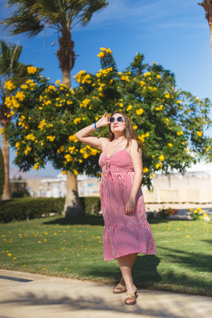 A young woman poses confidently in a beautiful pink dress while enjoying the bright, warm sunshine outdoorsの写真素材