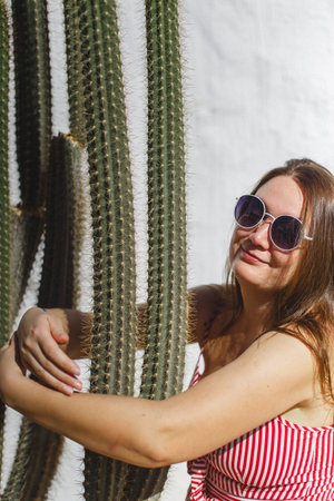 In a whimsical scene, a woman joyfully embraces a cactus, perfectly capturing the carefree essence of summer vibesの写真素材