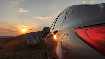 A stylish and modern car beautifully reflects the golden glow of a stunning sunset in an enchanting landscapeの写真素材