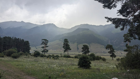 A stunning view of majestic mountains and lush fields under dramatic skies, capturing natures serene...